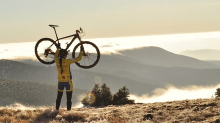 Bicycle rider holding bicycle in the air on top of a mountain