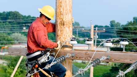 Worker fastening electrical wiring on street pole