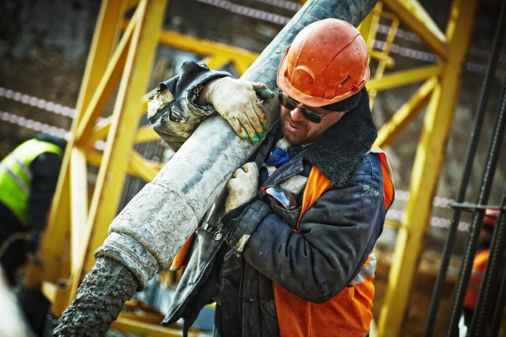 Construction worker in orange safety gear guiding flow of concrete.